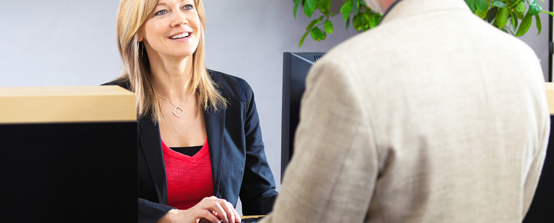 A female bank teller assists a male customer at the front desk.