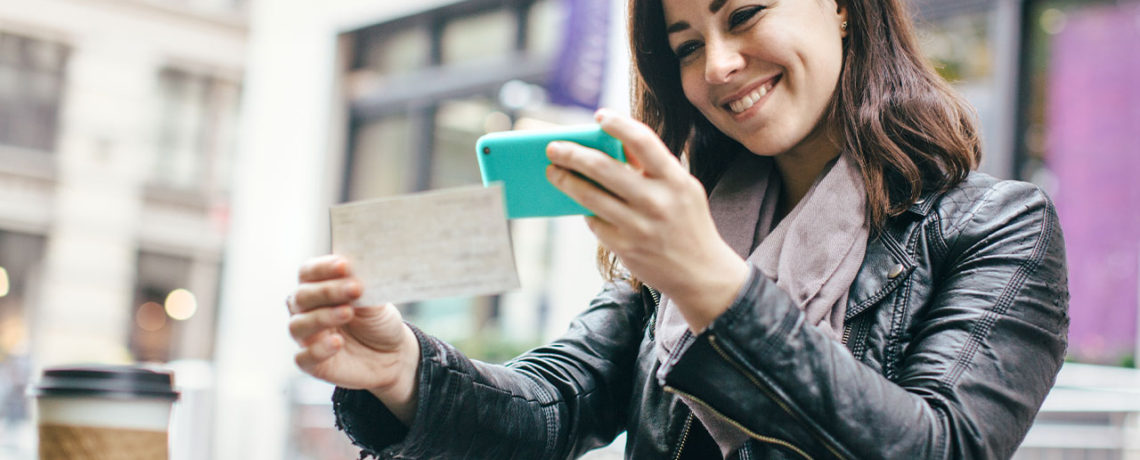 Woman sitting in park takes a picture of a check with her phone for mobile deposit