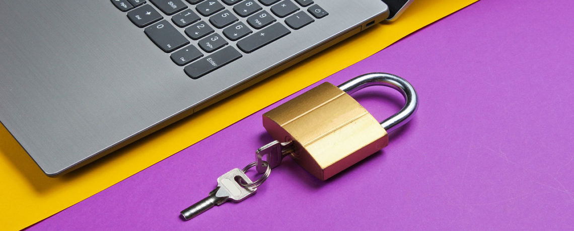 A padlock and key sit next to a laptop to represent identity theft prevention