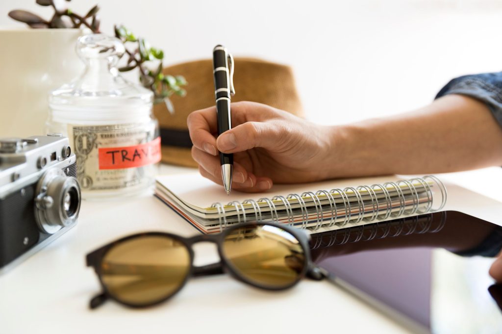 A person writes out their summer travel plans on a notebook.