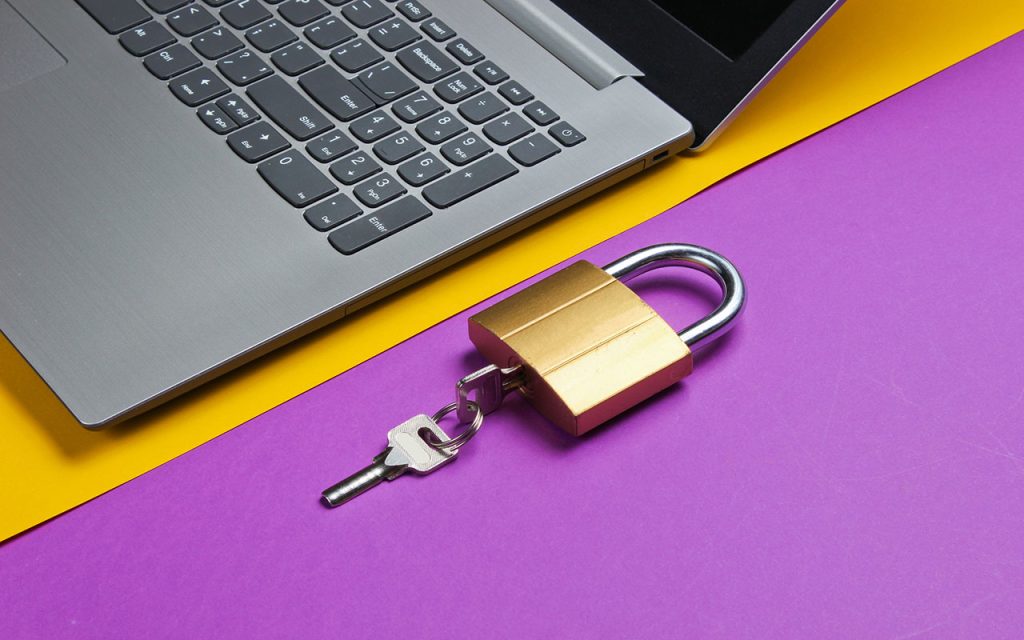 A padlock and key sit next to a laptop to represent identity theft prevention