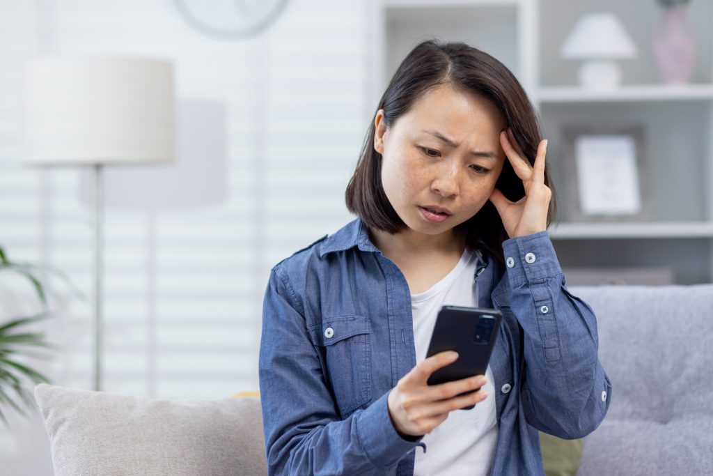 Young woman upset and looking at her smartphone after learning she's been hit with an investment scam